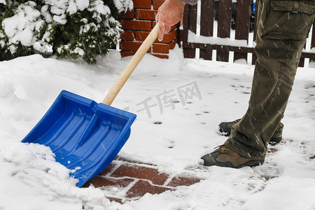 铲雪摄影照片_在暴风雪后从人行道上除雪的人