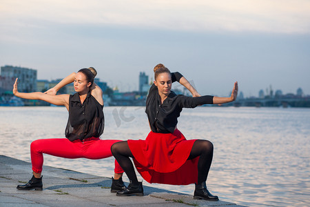 几何城市摄影照片_两个年轻漂亮的双胞胎姐妹在河附近的城市背景中起舞，waacking 舞蹈.