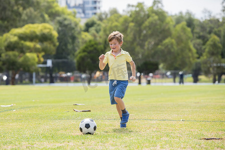 快乐体育活动摄影照片_小孩子7或8岁享受快乐踢足球足球在草市公园田野奔跑和踢球兴奋的童年运动激情