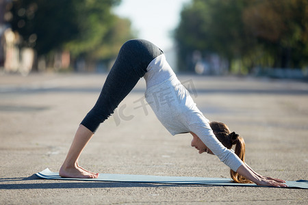 狗拉伸摄影照片_Street yoga: Downward facing dog pose