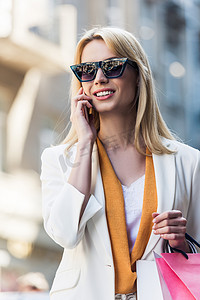 美丽的微笑的年轻妇女太阳镜购物袋智能手机