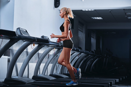快乐体育活动摄影照片_年轻漂亮的女人在健身房的跑步机上