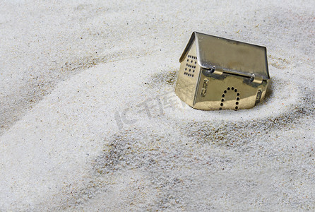 投资骗局摄影照片_小的金色模型房子下沉入沙子，风险的概念