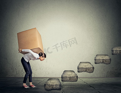 Difficult task concept. Young woman carrying heavy box upstairs