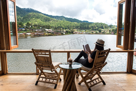 阅读本书，躺着的女人和喝冰咖啡在抵抗外力木阳台的椅子上美丽在内、 轻松和快乐的一天。生活方式的概念