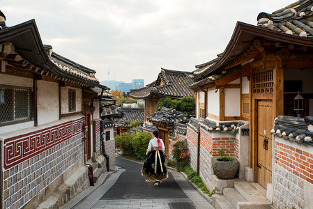建筑背景红色摄影照片_在韩国首尔 Bukchon 韩屋友楼村的首尔传统风格的房子里, 穿着韩的亚洲女人回来了。.