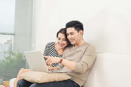 年轻的亚洲夫妇与便携式计算机在互联网上冲浪.