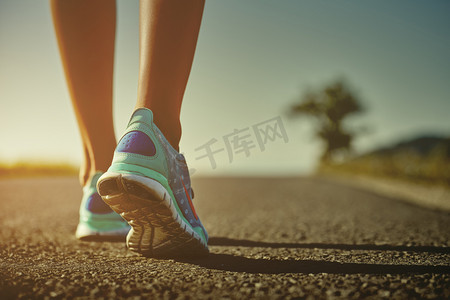 跑步女卡通摄影照片_女子赛跑运动员特写剃去在日出或日落的道路上跑步的跑步鞋的脚