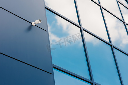 蓝色科技安全平台摄影照片_具有安全摄像头和反射云的现代办公大楼玻璃幕墙