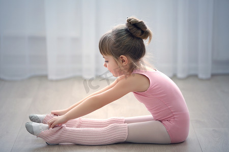 运动风格摄影照片_可爱的小女孩在粉红色紧身连衣裤在舞蹈工作室制作新芭蕾运动