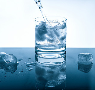 蓝色冷饮摄影照片_Water cold drink pouring into glass Blue colored