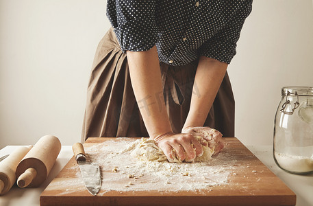 罗马人像摄影照片_Woman kneads dough for pasta on wooden board