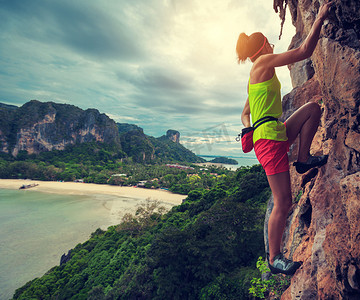 极限攀岩摄影照片_女人在海边悬崖攀登