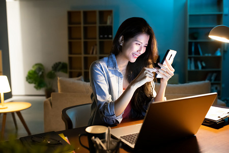 智能办公空间摄影照片_亚洲女商人使用智能手机和笔记本电脑在家工作