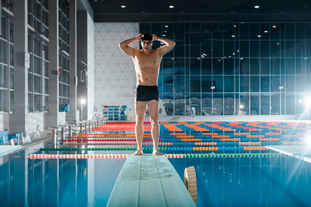 欧美体育摄影照片_在游泳池附近触摸泳帽的英俊而强壮的游泳运动员 