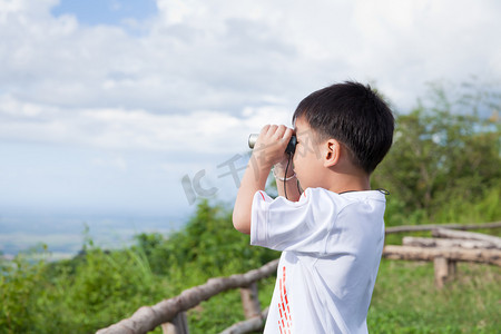 去旅行摄影照片_小的孩子看在双筒望远镜户外在阳光灿烂的夏天的一天 