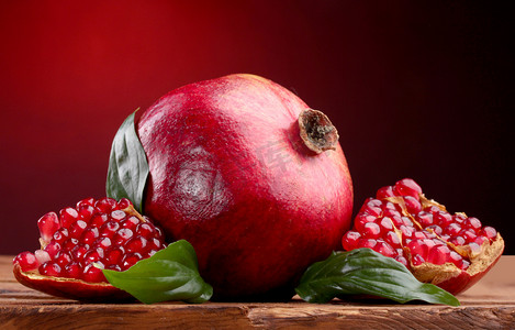 水果驿站摄影照片_与成熟的石榴果叶红色背景上的木桌上