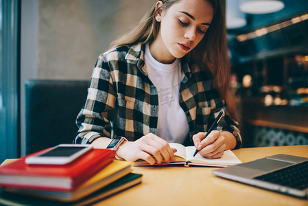 课程两折页摄影照片_认真的女性自由职业者花时间在大学图书馆, 而规划的工作过程在教科书, 有吸引力的集中妇女写审查访问自助餐厅在室内笔记本