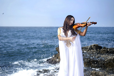 海面背景摄影照片_年轻有魅力的女人拉小提琴的海面背景