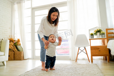 助发展摄影照片_Asian mother encouraging and helping her cute son learn to walk his first steps