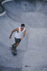 一个时髦的年轻人穿着白色 t恤, 在 skatepark 的滑板上溜冰, 在游泳池里滑冰。.