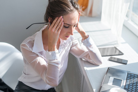 triste摄影照片_累了的年轻商界女强人患头痛在前面笔记本电脑在办公桌的肖像