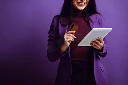 带着紫色背景的数码平板电脑和信用卡微笑的女人的剪影