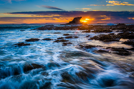 蓝色小浪花摄影照片_波浪和岩石在日落时，在日冕的小海滩，在电晕尼亚德尔