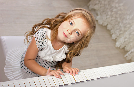 美丽的金发小女孩坐在附近一架钢琴的美人中