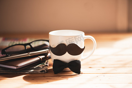 笔记书摄影照片_快乐的父亲日概念。咖啡杯与黑纸胡子和报纸, 笔记书, 杯子在木桌背景.