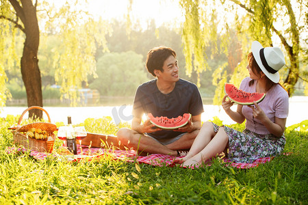 青年伴侣吃西瓜摄影照片_青年情侣坐在公园里吃西瓜