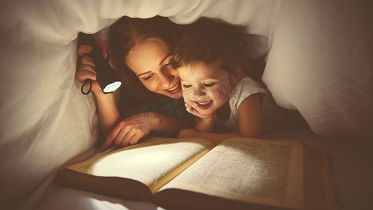 形象概念摄影照片_家庭阅读的就寝时间。妈妈和孩子读书与 flashl