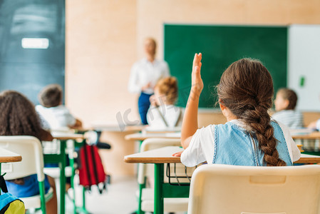 during摄影照片_back view of schoolgirl raising hand to answer teachers question during lesson