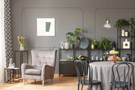 花植物海报摄影照片_米色扶手椅反对灰色墙壁与海报在平的内部与椅子在桌。真实照片