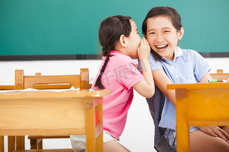 好玩摄影照片_快乐的小女孩耳语和分享在教室里的秘密