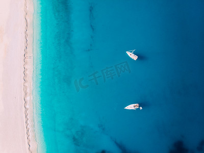 夏季沙滩游泳摄影照片_希腊密尔托斯，白色沙滩附近，有两艘游艇停靠在海面上