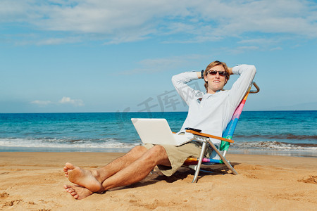 便携式摄影照片_有吸引力的年轻人放松在沙滩上与便携式计算机