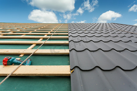 盖屋顶的人摄影照片_在建的房屋。屋顶用金属瓦、 螺丝刀和屋面铁
