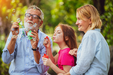 免费公益活动摄影照片_快乐的家庭在夏天周末去花园公园度假时一起吹肥皂泡。儿童教育和家庭活动概念.