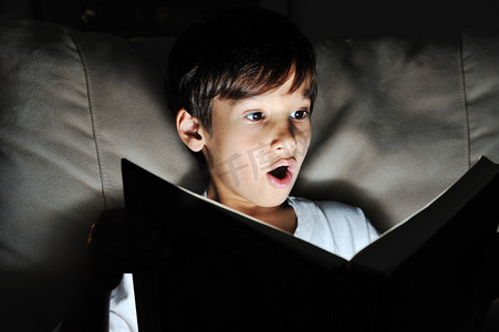 光魔法摄影照片_光在黑暗中感到震惊的孩子读的书