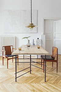 厨房白色摄影照片_优雅典雅的用餐室内饰，配有设计共享桌、椅子、金色花灯、抽象绘画和时尚配饰。花瓶里的热带叶子。装饰独特。棕色木制镶木地板.