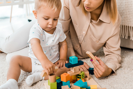 可爱的幼儿玩五颜六色的立方体和母亲在托儿所房间的裁剪视图