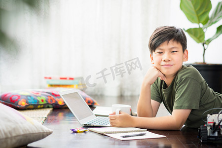 无聊暑假摄影照片_聪明英俊的亚洲未成年男孩躺在地板上带着自信和快乐微笑城市封锁和社会疏远措施而在家学习