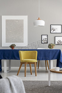 grey摄影照片_Yellow wooden chair at table with blue cloth in modern dining room interior with mockup. Real photo