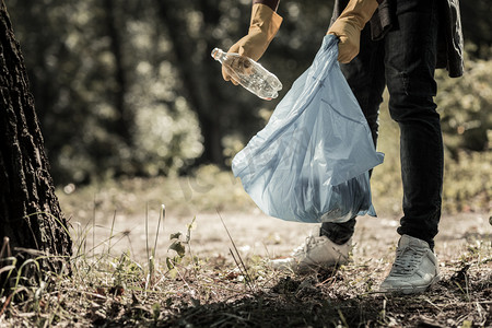 worker摄影照片_年轻的瞳孔穿牛仔裤和运动鞋收集空瓶子在森林里