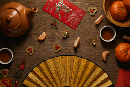 春节金币摄影照片_木桌上新鲜成熟的橘子、茶具、带象形文字和金币的扇子的顶部视图 