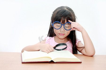 快乐的小亚洲女孩读本书戴着蓝色的眼镜，回