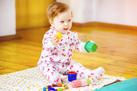 可爱的婴儿女孩坐在地板上玩玩具积木