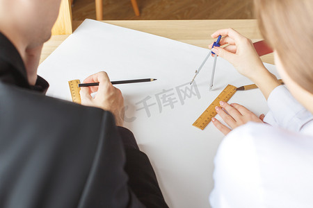 后视图绘制蓝图，使用标尺、 圆规和铅笔的男性和女性的手。在办公室的年轻建筑师