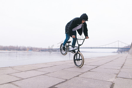 骑自行的男孩摄影照片_自由式自行车。一个年轻人正在河边的一辆小摩托自行车上玩把戏。